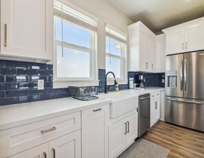 A modern kitchen with white cabinets, a stainless steel refrigerator, and a blue-tiled backsplash. - Bayfront Nirvana! by Ryson Vacation Rentals (Galveston)