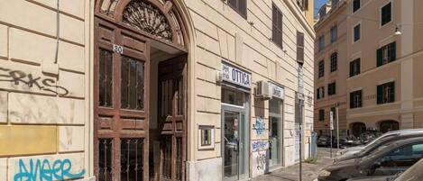A building with a large arched entrance, a shop named 'Ottica,' and a street with parked cars.