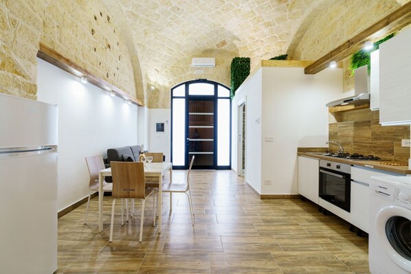 A modern kitchen with a stone ceiling, a dining area with a table and chairs, and a view of a staircase leading to an upper level.