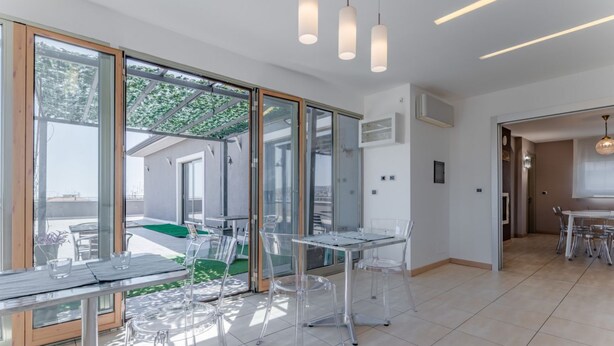 Ein modernes Interieur mit Glastüren, die zu einem Außenbereich führen, klaren Stühlen und einem Tisch.