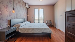 Ein Schlafzimmer mit Bett, Nachttischen, einem Sessel, einem Kleiderschrank und Blick durch eine Tür.