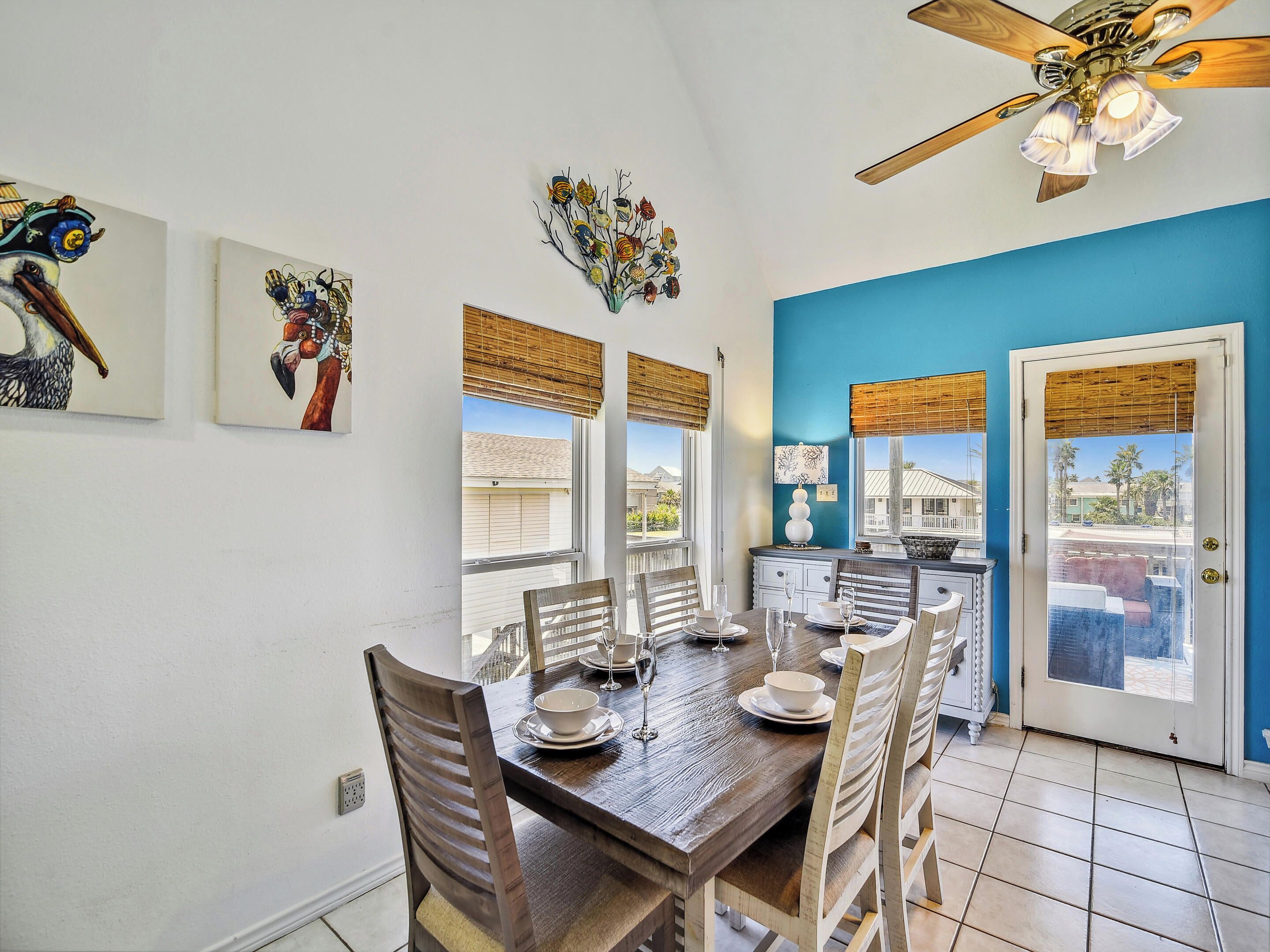 A dining area with a wooden table set for four, flanked by chairs, and a ceiling fan above.