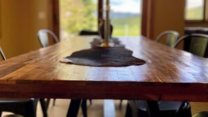 A wooden dining table with chairs, a central decorative item, and a view of a green landscape through a window. - Cozy Home steps from Town Center, with a Stunning View of the Mountains! (Big Sky)