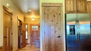 A kitchen with wooden cabinets, a stainless steel refrigerator, and a hallway with wooden doors. - Cozy Home steps from Town Center, with a Stunning View of the Mountains! (Big Sky)