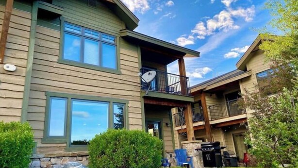 A two-story house with a balcony, stone steps, and a grill area. - Cozy Home steps from Town Center, with a Stunning View of the Mountains! (Big Sky)