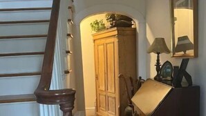 A staircase with wooden steps and a handrail, leading to a room with a wooden cabinet, a radiator, and a lamp on a table. - House in Newport (Newport)