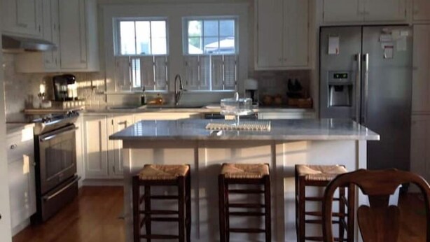 A spacious kitchen with a large island, wooden stools, and a refrigerator. - House in Newport (Newport)