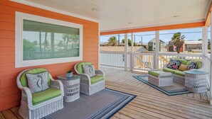 Ein überdachter Außenbereich mit Korbmöbeln, Blick auf den Strand und einer Holzterrasse.