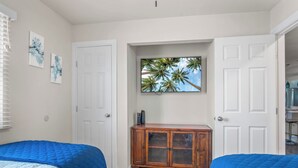 Ein Schlafzimmer mit zwei Betten, einem Holzschrank und einem großen Fenster mit Blick auf Palmen.