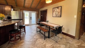 A kitchen with a wooden ceiling, a dining area with a bench and chairs, and a large window. - Royal Cabin between Lake Quachita and Hot Springs  (Royal)