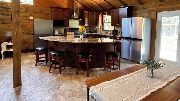 A rustic kitchen with a large island, wooden bar stools, and a refrigerator. - Royal Cabin between Lake Quachita and Hot Springs  (Royal)