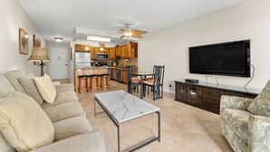 A living room with a sofa, a coffee table, a TV, and a kitchen in the background. - Kihei Akahi D-104 (Kihei)
