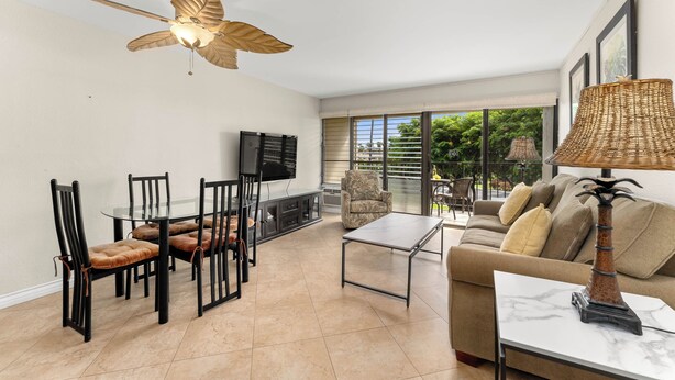 A living room with a ceiling fan, a TV, a sofa, a coffee table, and a dining area with chairs and a glass table. - Kihei Akahi D-104 (Kihei)
