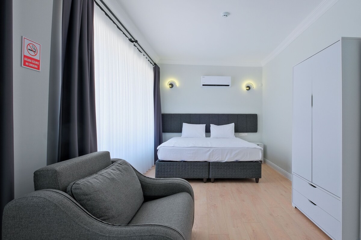 Une chambre d’hôtel avec un lit, un canapé gris, une armoire et un panneau indiquant qu’il est interdit de fumer.