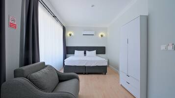 Una habitación de hotel con una cama, un sofá gris, un armario y un cartel de no fumar.