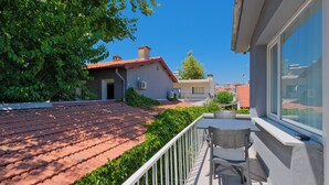 A balcony with a tiled roof, a chair, and a window overlooking a residential area with houses and greenery. - Central Flats Fethiye (Fethiye)
