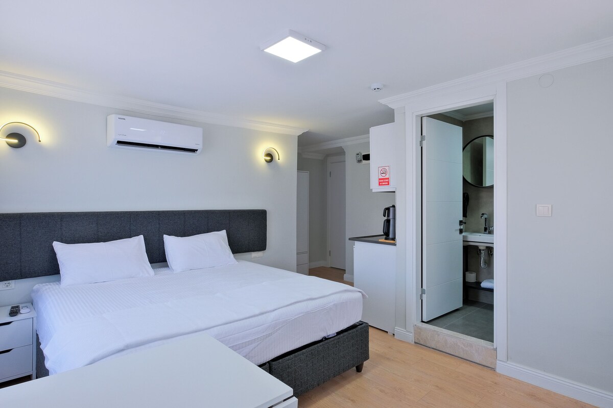 Une chambre d’hôtel moderne dotée d’un grand lit, de tables de chevet, d’un radiateur intégré, d’une machine à café et d’une salle de bain avec un miroir et un lavabo.