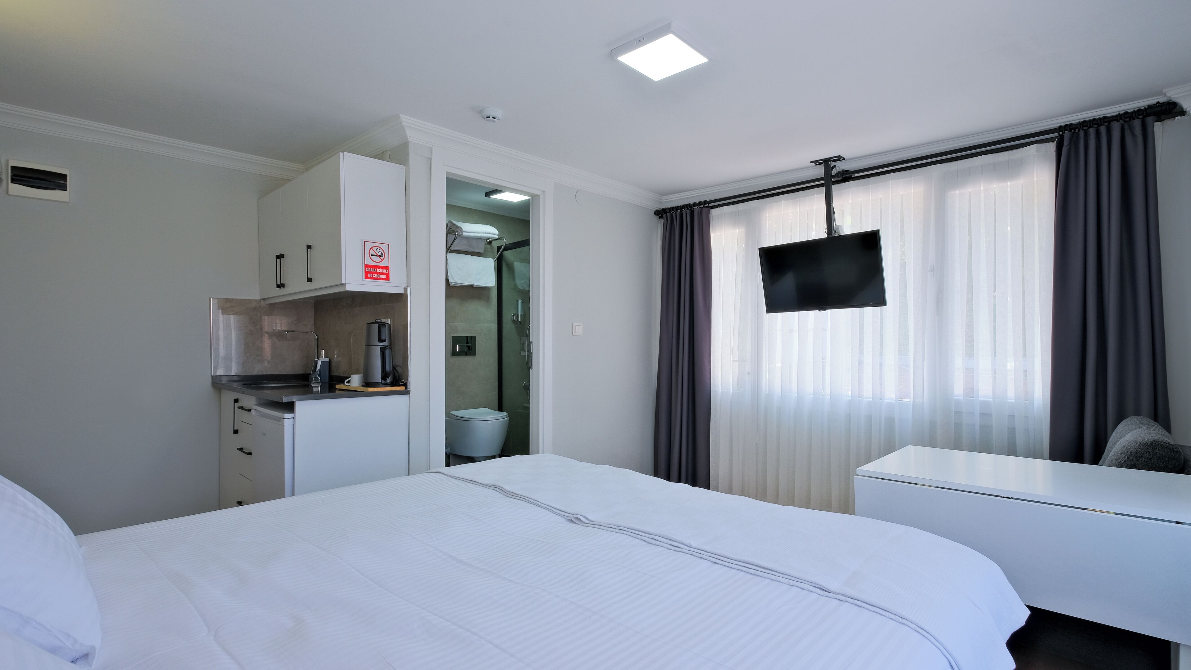 Una habitación de hotel con cama, escritorio, kitchenette, televisor y baño.
