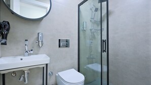 A modern bathroom with a glass-enclosed shower, a white sink, and a toilet. - Central Flats Fethiye (Fethiye)