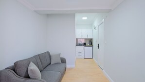 A modern apartment with a grey sofa, a kitchen with white cabinets, and a wooden floor. - Central Flats Fethiye (Fethiye)