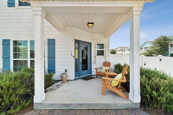 A covered porch with two wooden Adirondack chairs and a blue door.