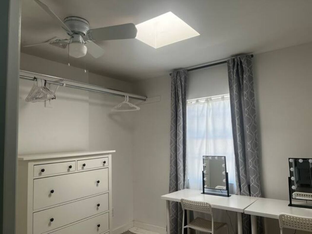 Une chambre à coucher comprenant un lit, un bureau, une chaise, une armoire et un ventilateur de plafond.