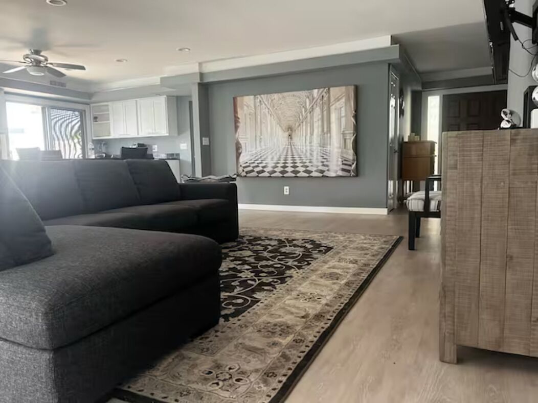 Un salon moderne avec un canapé gris, un tapis à motifs et une grande œuvre d’art accrochée au mur.