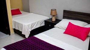A hotel room with two beds, each with white bedding and a red pillow. There is a nightstand with a lamp between the beds. - Hotel Ruta Del Mar (Santa Marta)