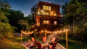 Eine zweistöckige Holzhütte mit einer Terrasse, umgeben von Bäumen und Lichterketten.