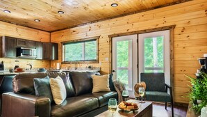 Ein gemütliches Blockhaus-Interieur mit einem Ledersofa, einem Esstisch mit Weingläsern und einer Küchenzeile mit Mikrowelle.