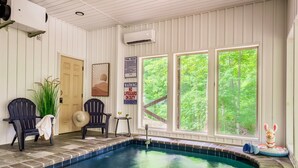 Ein Hallenbad mit Blick auf Bäume, zwei Adirondack-Stühle, ein Ventilator und ein Rettungsschwimmer-Schild.