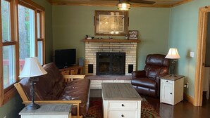 Una sala de estar acogedora con chimenea, muebles de cuero y un ventilador de techo.