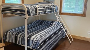 Habitación con literas, suelo de madera y dos ventanas con persianas.