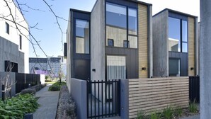 Ein modernes Wohnhaus mit zwei Stockwerken, großen Fenstern, einer Holzterrasse und einem schwarzen Metallzaun.