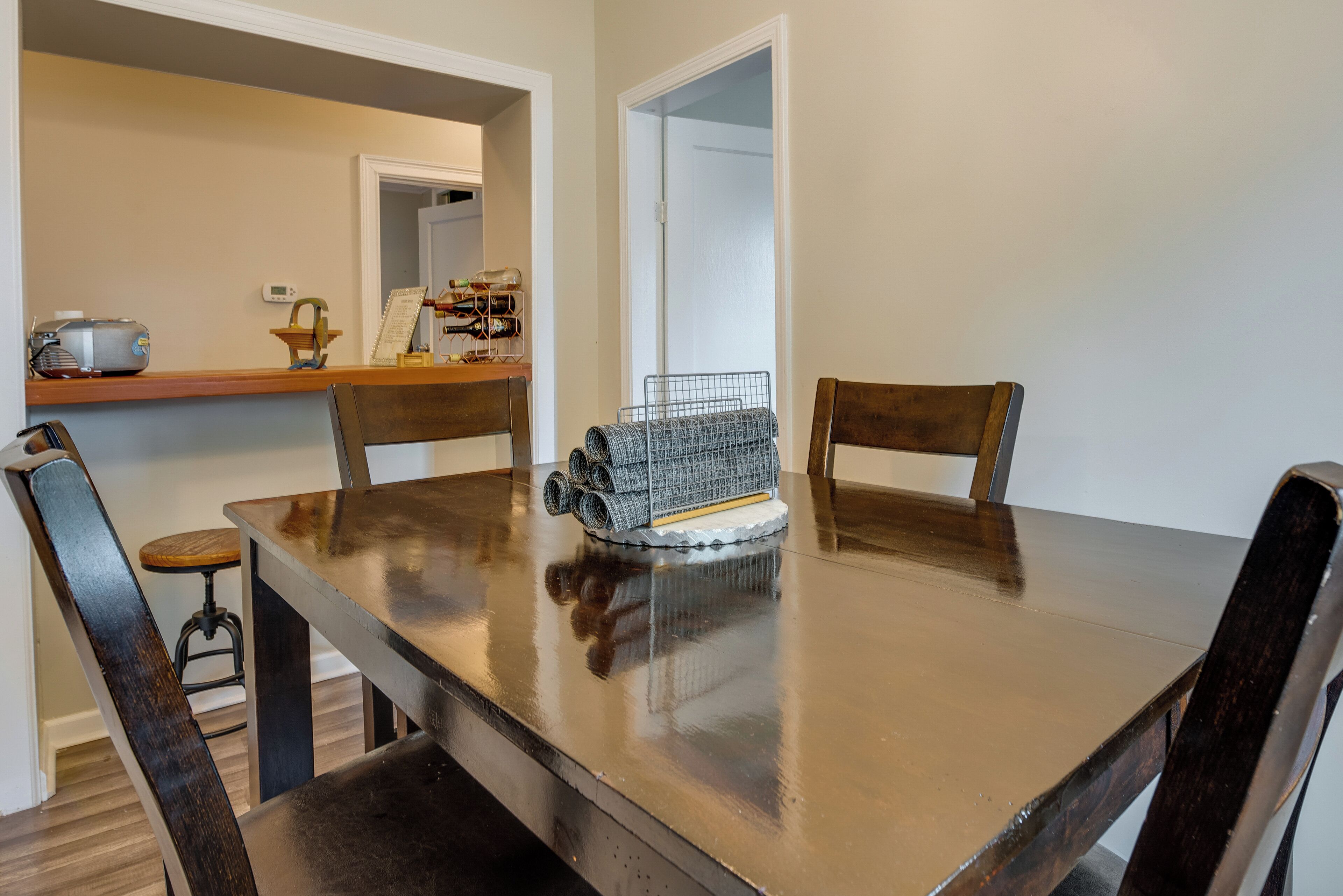 A dining table with chairs, a small kitchen area with a toaster and a wine rack, and a doorway leading to another room.