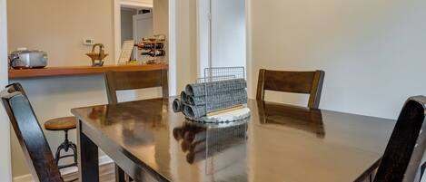 A dining table with chairs, a small kitchen area with a toaster and a wine rack, and a doorway leading to another room.