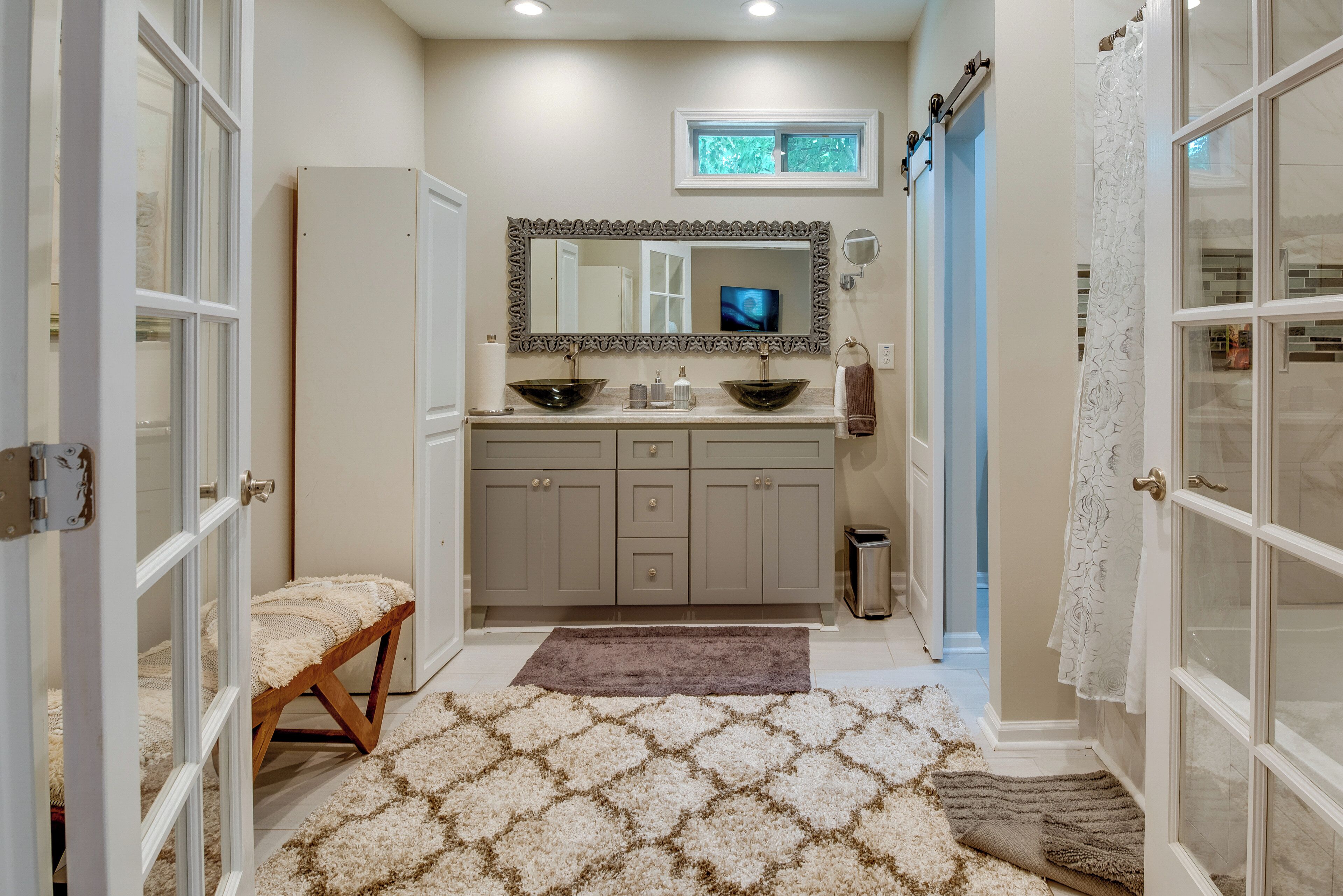 A bathroom with a vanity, two sinks, a mirror, a window, and a bench.