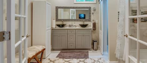 A bathroom with a vanity, two sinks, a mirror, a window, and a bench.