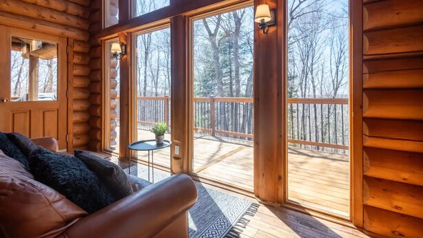 A log cabin interior with a large window, a wooden deck, and a leather sofa. - 7BR LogCabin/Spa/Nature/MontTremblant Area/18 Guests  (Labelle)