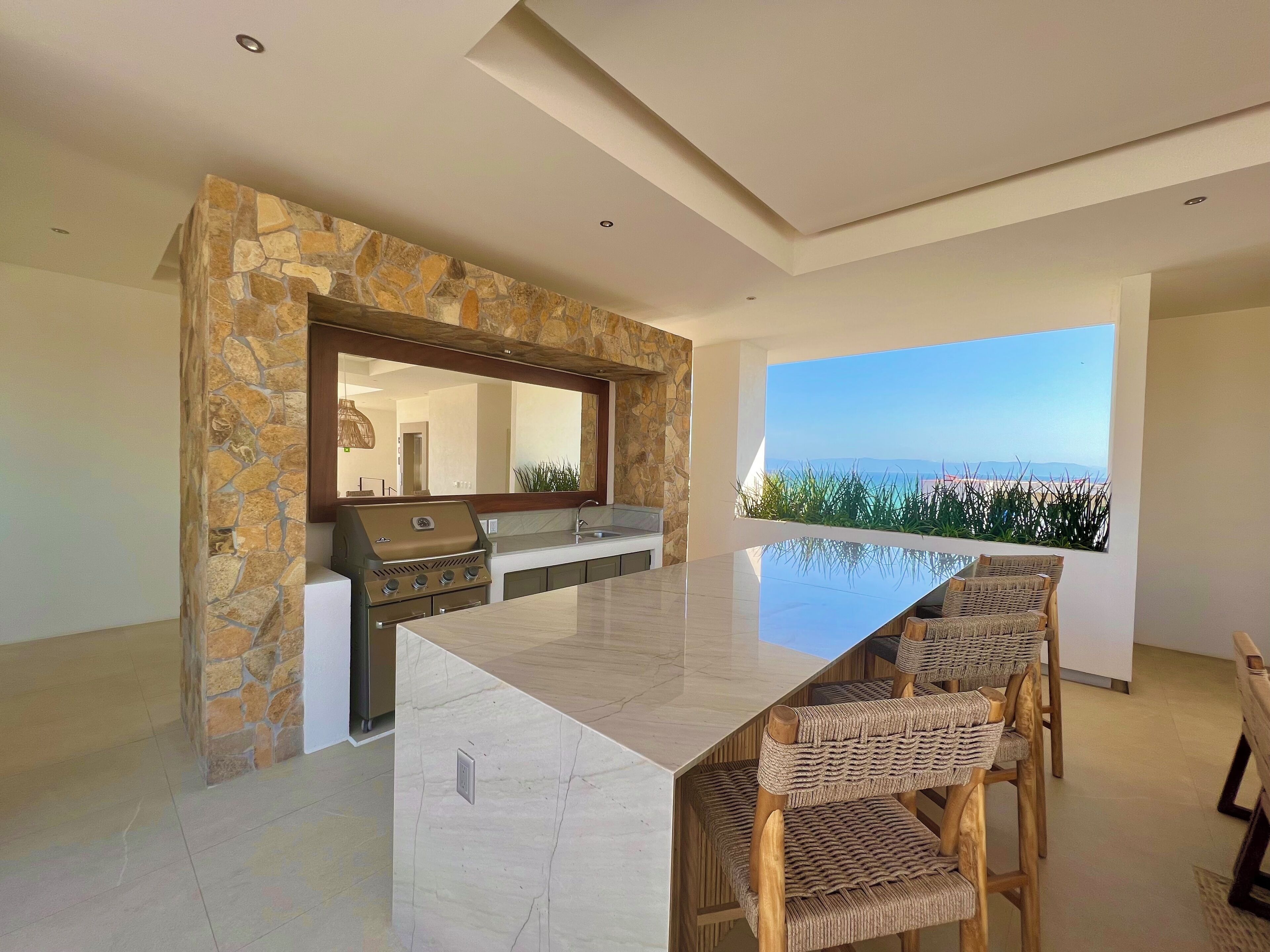 Una cocina moderna con una pared de acento de piedra, una isla grande con taburetes de bar y vistas al océano.
