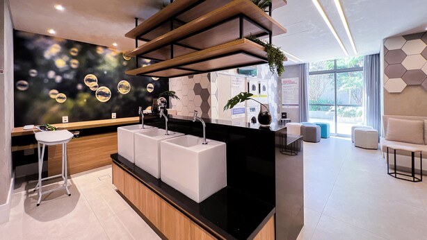 A modern reception area with a black countertop, three white sinks, and a wooden shelf with plants. - New studio in Pinheiros - Great Location - comfort - safety (Pinheiros São Paulo)