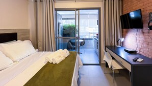A hotel room with a bed, a desk, a TV, and a sliding glass door leading to a balcony. - New studio in Pinheiros - Great Location - comfort - safety (Pinheiros São Paulo)