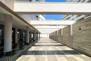 Un pasillo cubierto con suelo de baldosas, columnas y fachada de edificio al fondo.