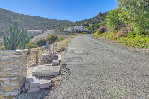 A rural road with a house in the distance, surrounded by greenery and hills. - Mountain-Top Retreat with Private Sunset Patio & Epic Views (newbury park)