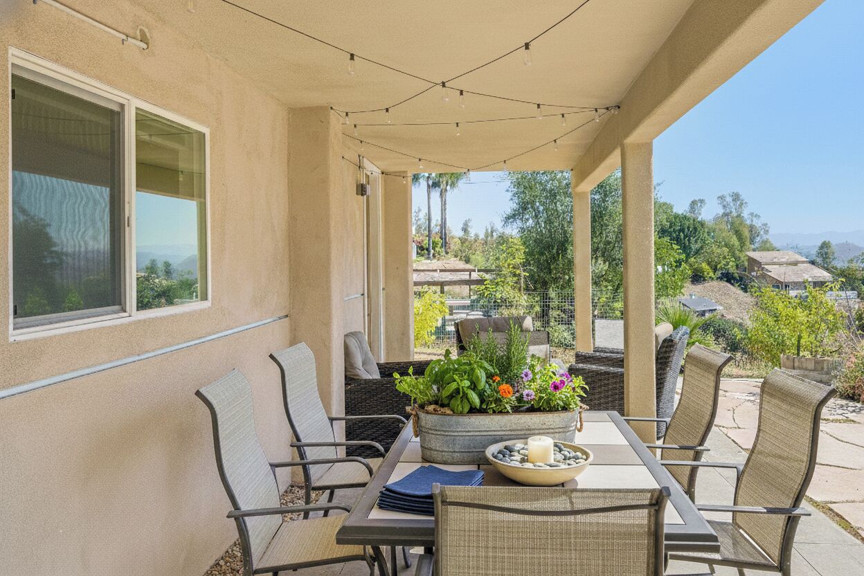 An outdoor patio with a table and chairs, a planter with flowers, and a view of the surrounding neighborhood.