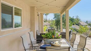An outdoor patio with a table and chairs, a planter with flowers, and a view of the surrounding neighborhood.