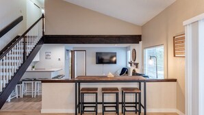 A modern kitchen with a central island, bar stools, and a staircase leading to an upper level.