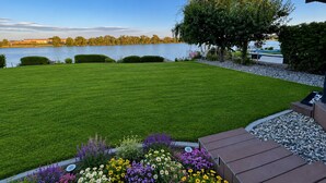 A well-maintained lawn, a flower bed with various flowers, and a view of a lake with a boat dock.