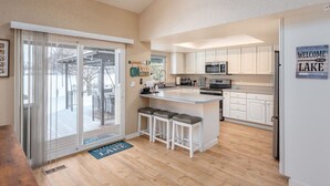 A modern kitchen with white cabinets, a central island with stools, and a large window overlooking a deck.