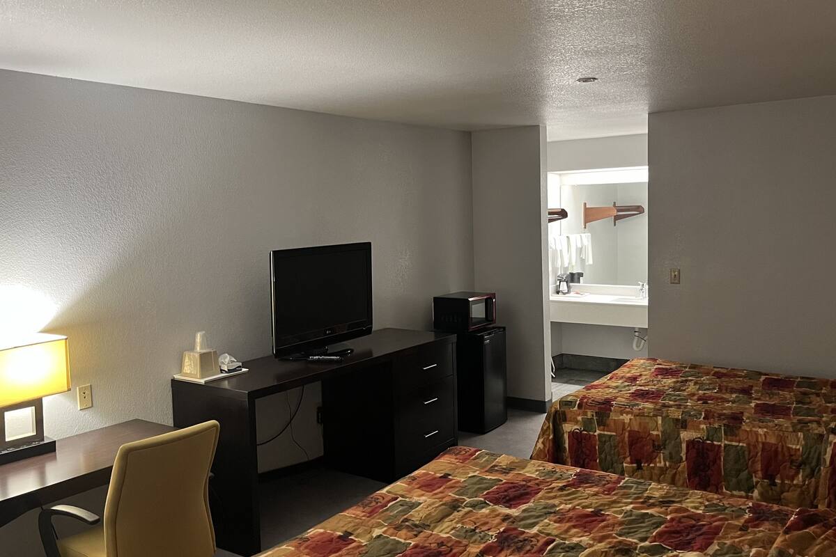 Une chambre d’hôtel équipée d’un bureau, d’une télévision, d’un lit avec une couvre-lit à motifs et d’une salle de bain visible à travers une porte ouverte.
